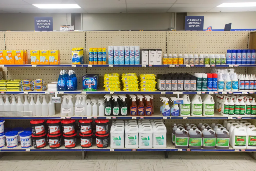 Cleaning supplies such as bleach, Lysol, spray bottles and scrub brushes sitting on shelves..
